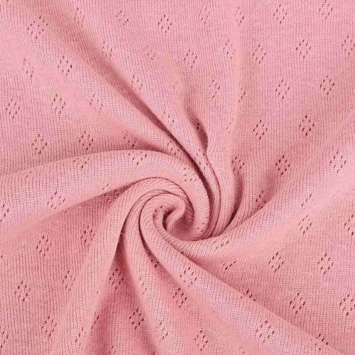 French rose pink pointelle knit jersey fabric from Once Upon A Fabric with diamond-shaped perforations. The pointelle cotton jersey fabric appears lightweight, suggesting it may be perfect for baby clothes or accessories.