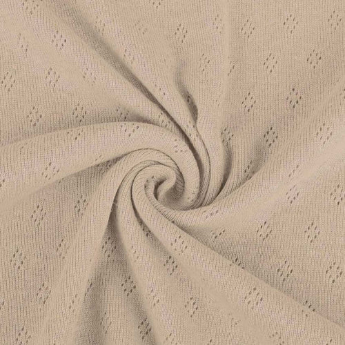 Taupe light brown pointelle knit jersey fabric from Once Upon A Fabric with diamond-shaped perforations. The pointelle cotton jersey fabric appears lightweight, suggesting it may be perfect for baby clothes or accessories.