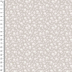 A swatch of Oeko-Tex 100 certified fabric featuring a small, white floral pattern on a soft beige background. A white ruler with black markings is placed vertically on the left side, measuring up to 18 centimeters. This Cotton Jersey Fabric - Millefleur Taupe by Once Upon A Fabric is perfect for dressmaking projects.