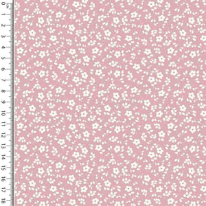 A pink dressmaking fabric with a white floral pattern. A ruler is placed along the left side of the Cotton Jersey Fabric - Millefleur Old Rose by Once Upon A Fabric, showing measurements from 1 to 18 inches. This Oeko-Tex 100 certified fabric ensures quality and safety in your projects.