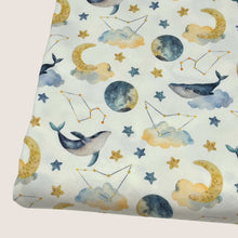 Load image into Gallery viewer, A piece of Cotton Jersey Fabric - Moon Whales by Once Upon A Fabric featuring a whimsical print with moons, stars, clouds, constellations, and whales on a light background. The design includes watercolor-style illustrations in shades of blue, yellow, and gray, perfect for creating adorable baby clothes. Oeko-Tex 100 certified.
