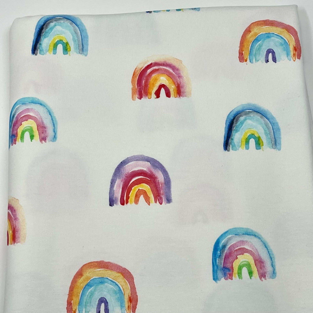 This Once Upon A Fabric LAST METER Cotton Jersey Fabric - Bright Rainbows is decorated with a pattern of small, colorful rainbows. The rainbows, in varying shades of blue, green, yellow, red, purple, and pink, are evenly spaced across the fabric. Perfect for dressmaking projects.