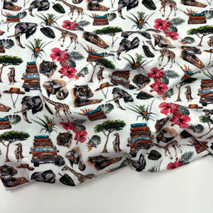 A digitally printed **Once Upon A Fabric LAST METER Cotton Jersey Fabric - Holiday** with a colorful design featuring jungle animals, trees, tropical flowers, and vintage vehicles. The detailed illustrations of elephants, giraffes, zebras, and tigers are highlighted against a white background. Plus, it’s Oeko-Tex 100 certified for added assurance.