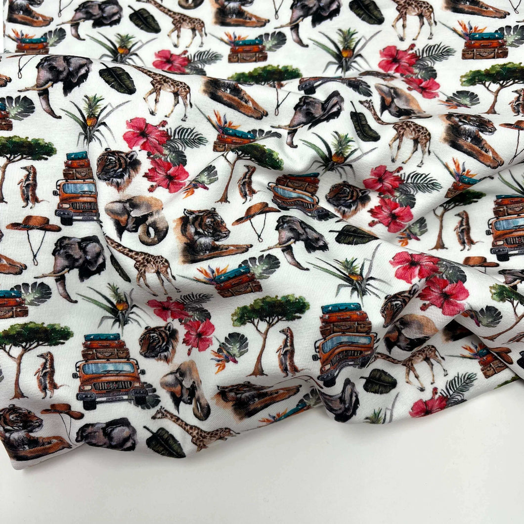 A digitally printed **Once Upon A Fabric LAST METER Cotton Jersey Fabric - Holiday** with a colorful design featuring jungle animals, trees, tropical flowers, and vintage vehicles. The detailed illustrations of elephants, giraffes, zebras, and tigers are highlighted against a white background. Plus, it’s Oeko-Tex 100 certified for added assurance.