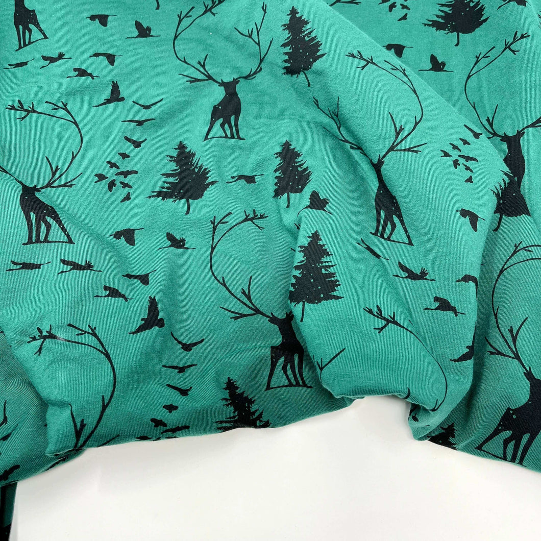 Green French Terry fabric with a Woodland print of black silhouettes, including deer, trees, and birds. This Oeko-Tex 100 certified fabric is slightly crumpled and displayed on a flat surface. This product is called LAST METER French Terry Fabric - Woodland Dark Green by Once Upon A Fabric.