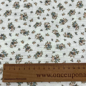 A beige Organic Muslin Fabric / Double Gauze Fabric - Mini Flowers Blue with a small floral pattern in blue, green, and pink is displayed with a wooden ruler at the bottom showing centimeters and millimeters. The ruler reads "Once Upon A Fabric" along the length.