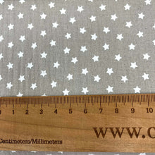 Load image into Gallery viewer, Close-up of a Muslin Fabric / Double Gauze Fabric - Mini Stars Taupe by Once Upon A Fabric with a pattern of small white stars on a gray background. A wooden ruler with measurements in centimeters and millimeters is placed on the muslin fabric, showing a length of approximately 15 centimeters.
