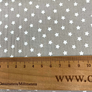 Close-up of a Muslin Fabric / Double Gauze Fabric - Mini Stars Taupe by Once Upon A Fabric with a pattern of small white stars on a gray background. A wooden ruler with measurements in centimeters and millimeters is placed on the muslin fabric, showing a length of approximately 15 centimeters.
