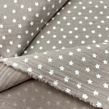 Load image into Gallery viewer, A close-up image of Muslin Fabric / Double Gauze Fabric - Mini Stars Taupe by Once Upon A Fabric with a grayish-brown background featuring a pattern of small white stars. The Muslin Fabric / Double Gauze Fabric - Mini Stars Taupe is layered, with the edges slightly frayed.
