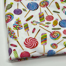 Load image into Gallery viewer, This Organic GOTS Cotton Jersey - Lollipops by Once Upon A Fabric boasts a vibrant candy pattern with lollipops, swirled candies, and striped stick candies in red, green, blue, and pink on a white background. Perfect for baby clothes fabric applications, it comes neatly folded.
