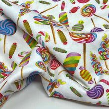 Load image into Gallery viewer, A fabric with a colorful candy-themed print, perfect for baby clothes. The pattern features various candies including lollipops, candy canes, and wrapped sweets in vibrant shades of red, blue, green, yellow, and pink on a white background. Made from organic cotton and GOTS certified for safety and quality—Once Upon A Fabric&#39;s Organic GOTS Cotton Jersey - Lollipops.
