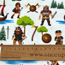 Load image into Gallery viewer, Organic cotton jersey fabric featuring Vikings, longships, dragons, treasure chests, axes, pine trees, and shields. The elements are scattered across a white background with some Vikings holding weapons and two green dragons depicted.
