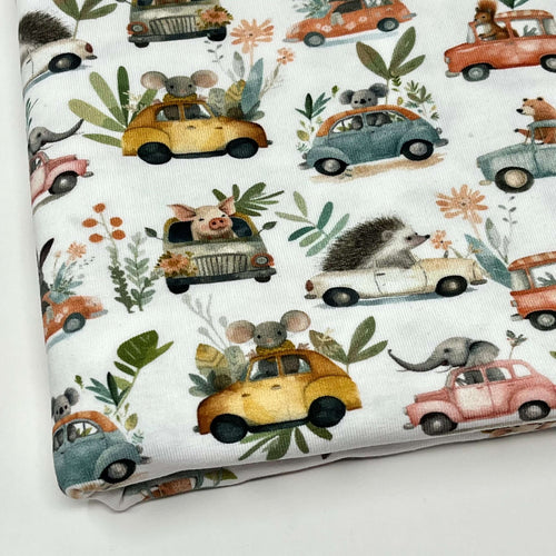 Organic GOTS Cotton Jersey with a whimsical pattern featuring small animals driving colourful cars. The digitally printed design includes mice, rabbits, hedgehogs, and elephants, surrounded by various plants and flowers against a white background.