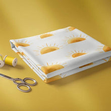 Load image into Gallery viewer, A neatly folded piece of white Jersey Fabric - SUNSET by Family Fabrics featuring a pattern of yellow rising suns is placed on a yellow surface. Beside it are two spools of yellow thread and a pair of metal scissors, perfect for crafting baby clothes that are Oeko-Tex 100 certified. This quality fabric is proudly brought to you by Once Upon A Fabric.
