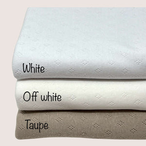 Three folded knit fabrics are stacked in a pile. The top fabric, perfect for baby clothes fabric, is labeled "Pointelle Jersey - White" from Once Upon A Fabric. The middle Oeko-Tex 100 certified fabric is labeled "Off white," and the bottom Pointelle cotton jersey is labeled "Taupe." Each fabric has a subtle textured pattern.