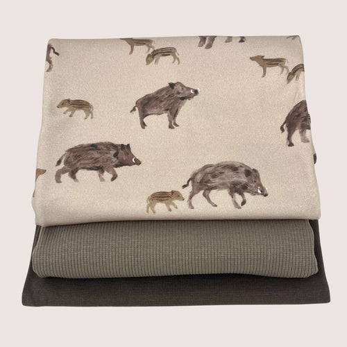Three folded fabric pieces are stacked. The top piece, an organic GOTS cotton jersey, features a print with illustrations of wild boars in various sizes. The middle piece is a plain, light grey rib knit jersey, and the bottom piece is a plain, dark grey fabric. The background is off-white. This Jersey Remnants Bundle 1.3 m from Once Upon A Fabric showcases the beautiful and varied selection of fabrics in this collection.