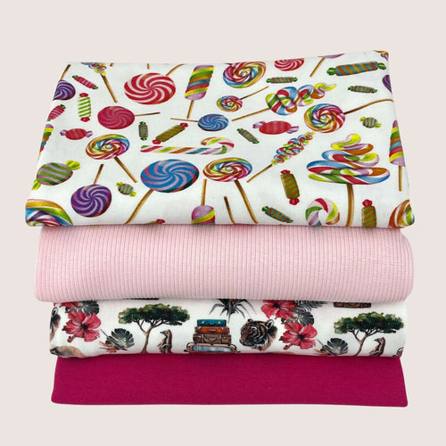 Four folded fabrics are stacked on top of each other. The top fabric features a colorful candy print, the second is a solid pink, the third has a scenic print with trees and vehicles, and the bottom fabric is in solid dark pink. Made entirely from organic cotton, these fabrics promise both comfort and quality. This Jersey Remnants Bundle 1.5 m by Once Upon A Fabric is perfect for your next sewing project.