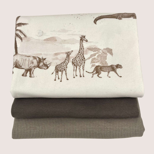 Three folded fabrics are stacked on top of each other. The top fabric, a cotton jersey, features a printed design of a rhino, two giraffes, and a cheetah against a landscape background. The middle fabric is solid dark brown, and the bottom one is fine rib knit in light brown. This collection is available as the Jersey Remnants Bundle 1.1 m from Once Upon A Fabric.