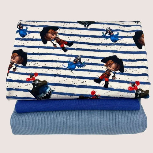 A stack of three folded fabrics: the top fabric, a playful pirate-themed cotton jersey with cartoon characters; the middle fabric, a solid dark blue; and the bottom fabric, a light blue with a subtle texture from the Jersey Remnants Bundle 1.4 m by Once Upon A Fabric.