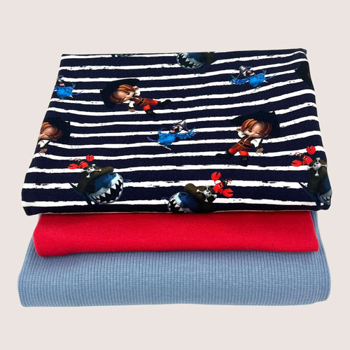 Three folded pieces of fabric are stacked. The top rib knit jersey has a navy blue and white striped pattern with cartoon characters and scenes. The middle fabric is solid red, and the bottom fabric is solid light blue. This collection is known as Jersey Remnants Bundle 1.4 m from Once Upon A Fabric.