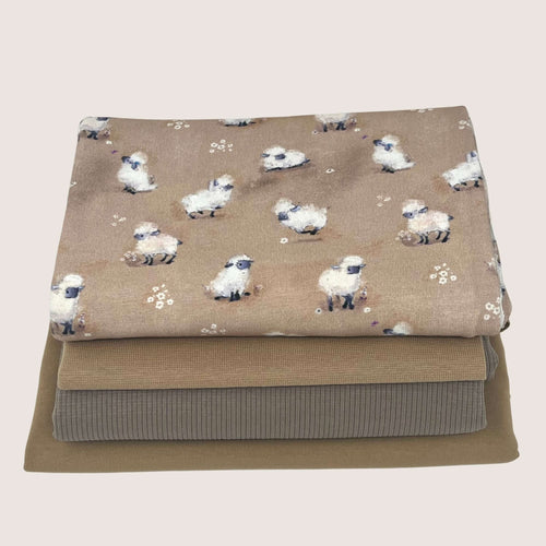A photo of three folded fabrics stacked on top of each other. The top fabric, a fine rib knit, features a pattern of sheep and small white flowers on a tan background. The middle and bottom fabrics are plain, neutral shades of beige and brown cotton jersey, respectively. This is the Jersey Remnants Bundle 1.5 m from Once Upon A Fabric.