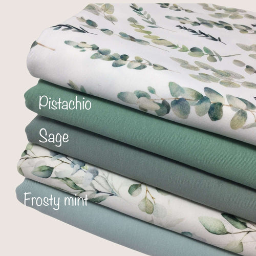 A stack of four folded baby clothes fabrics reveals their colors and patterns. The top cotton jersey fabric, labeled 