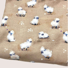 Load image into Gallery viewer, A light brown printed Cotton Jersey Fabric - Cute Sheep Beige from Once Upon A Fabric with a digitally printed pattern of small, white sheep scattered across. Some sheep are standing while others are sitting. Small, white flowers are interspersed among the sheep on the Oeko-Tex 100 certified fabric.
