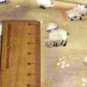 Baby fabric features a delightful pattern of small white sheep on a beige background, interspersed with tiny white flowers.