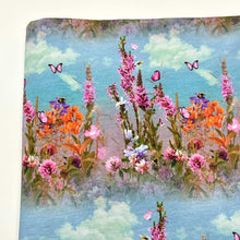 Load image into Gallery viewer, A piece of **Once Upon A Fabric LAST METER Jersey Fabric - Summer Meadow** with a floral pattern featuring various colorful flowers and pink butterflies against a blue sky with clouds. The flowers are in shades of orange, pink, purple, and green—perfect for baby clothes.
