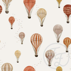 Patterned stretch cotton jersey fabric with gender neutral red and beige hot air balloons of various designs and colors drifting in the sky on an off white background, complemented by small, scattered birds. Family Fabrics Design in the UK.